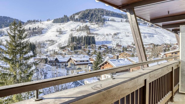 A snow-covered mountain village with wooden buildings and a wooden balcony railing.