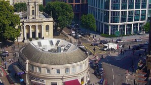 Un edificio histórico con una cúpula central y arquitectura clásica, rodeado de edificios modernos y una calle concurrida.