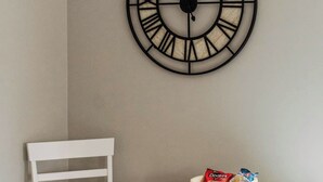 Et hvidt spisebord med en skål snacks, en hvid stol og et vægur.