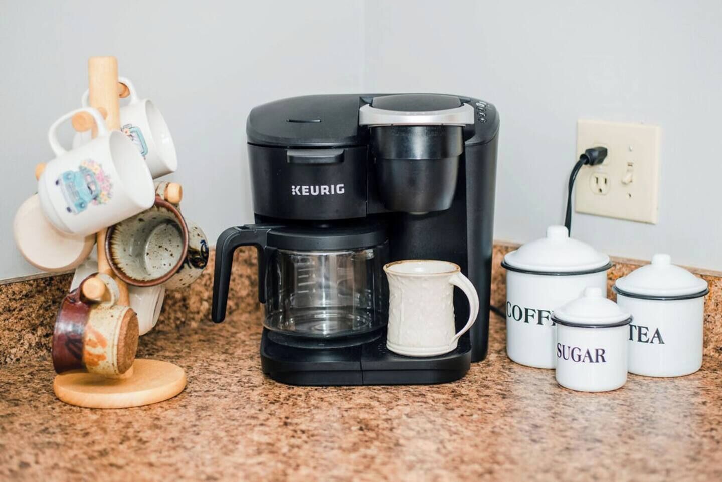 A coffee maker, a mug, and containers labeled with coffee-related items on a kitchen counter.