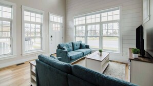 A spacious living room with a large window, a blue sofa, a coffee table, and a TV on a wooden stand.