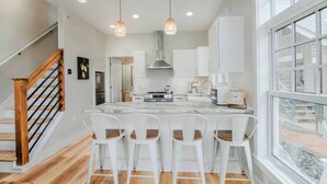 A modern kitchen with a marble island, white chairs, and pendant lighting.