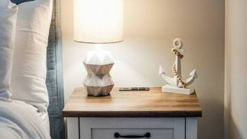 A neatly made bed with a headboard, a bedside lamp, a small wooden nightstand with drawers, and a decorative anchor.