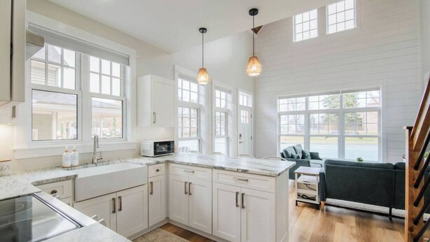 A modern kitchen with white cabinetry, a granite countertop, and a built-in microwave. There are large windows providing natural light and a view of the outdoors.