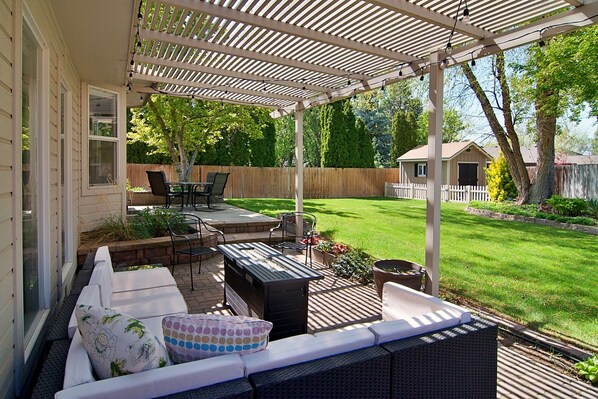 A covered patio area with outdoor furniture, a wooden fence, and a well-maintained lawn. - 5BR, Sleeps 12, Fire Pit, BBQ, Shaded Patio, Group Friendly Layout (Meridian)