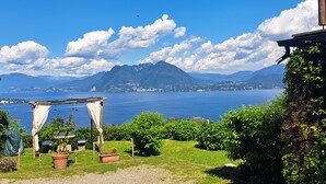A garden with a pergola, potted plants, and a view of a lake with mountains in the background. - ENCHANTING LOFT "Shambalahome.it" (STRESA)
