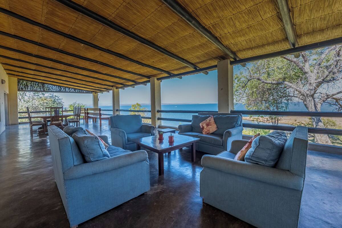 A covered outdoor seating area with blue sofas and a wooden table, overlooking a body of water.