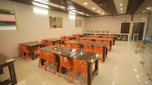 A dining area with multiple tables and chairs, a reception desk, and a glass partition. - Glorious Resort Rishikesh (Rishikesh)
