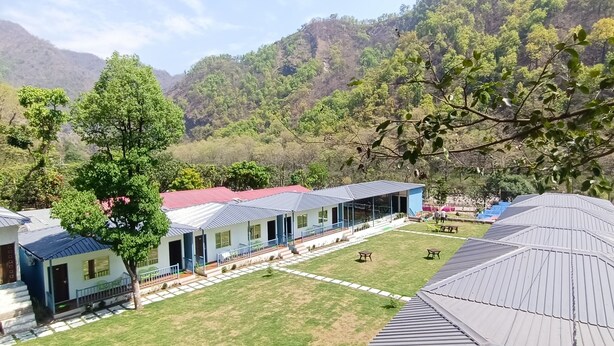 A row of cabins with a grassy yard and a mountain backdrop. - Glorious Resort Rishikesh (Rishikesh)