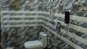 A bathroom with a marble wall, a white toilet, a sink, and a shower with a handheld showerhead. - Glorious Resort Rishikesh (Rishikesh)