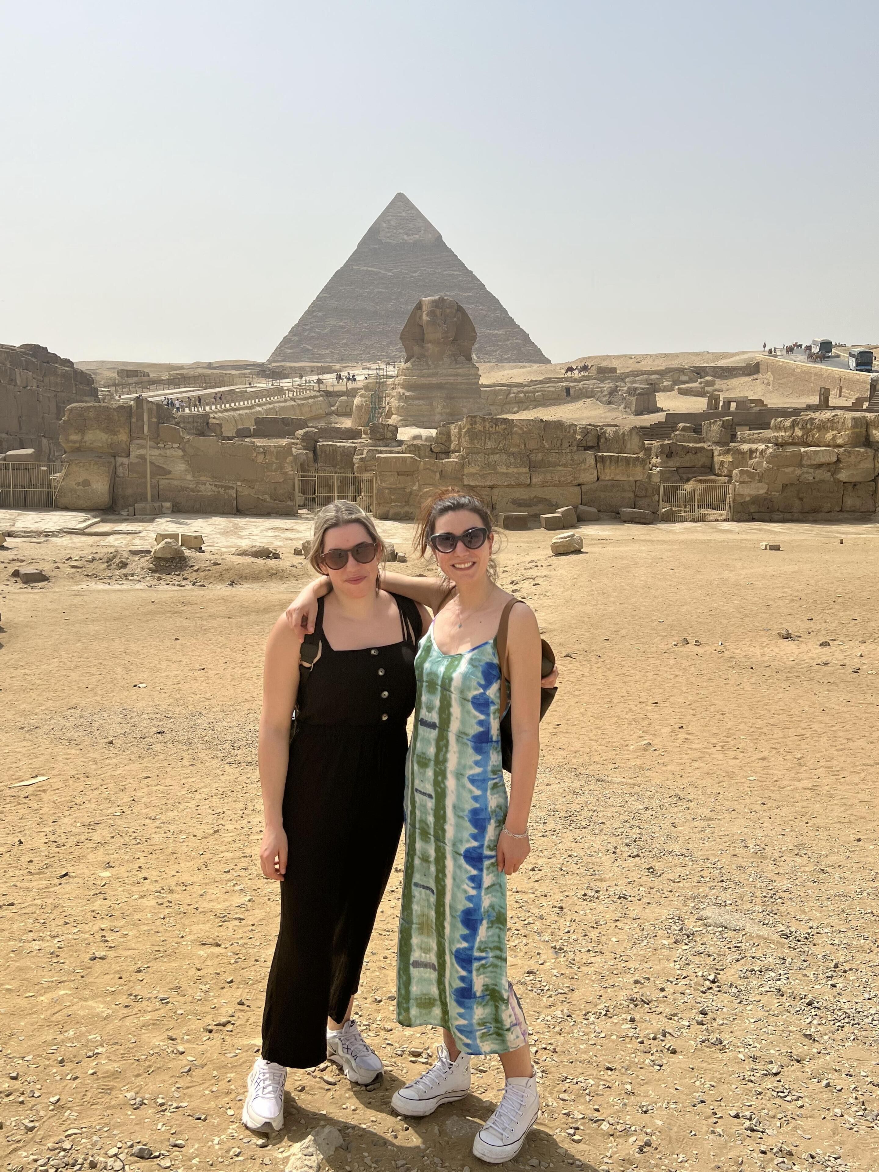 Två personer står framför den stora pyramiden i Giza, med antika ruiner i bakgrunden.