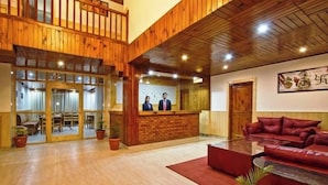 A lobby with wooden paneling, a reception desk, a red sofa, and potted plants. - Hayer Regency (Manali)