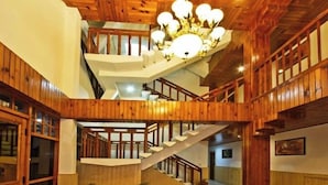 A multi-level wooden interior with a central staircase, wooden railings, and a chandelier. - Hayer Regency (Manali)