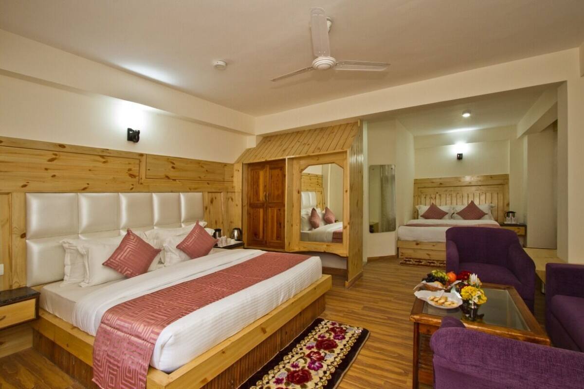 A bedroom with a large bed, wooden headboard, a ceiling fan, a mirror, a sofa, and a coffee table with a floral arrangement.