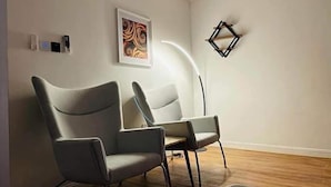 Quarto moderno com duas cadeiras cinzentas, piso de madeira, pintura abstrata emoldurada e decoração geométrica na parede.