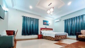 Quarto de hotel com cama, escrivaninha, cadeira e televisão.