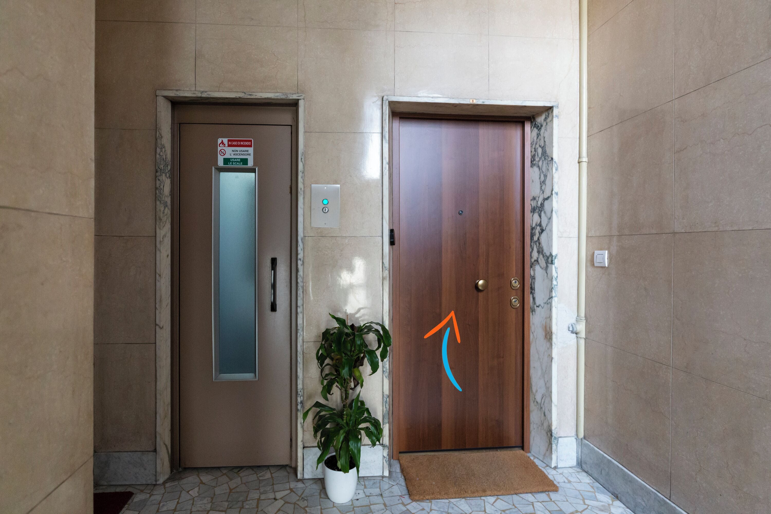 An elevator and a door with a doormat and a potted plant.