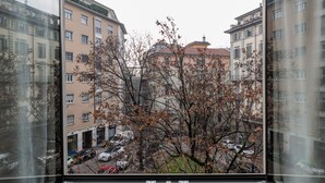 A view from a window of a multi-story building with parked cars in the foreground and a tree with autumn leaves in the middle ground. - notaMi - Arena Modern Apartment (Milan)