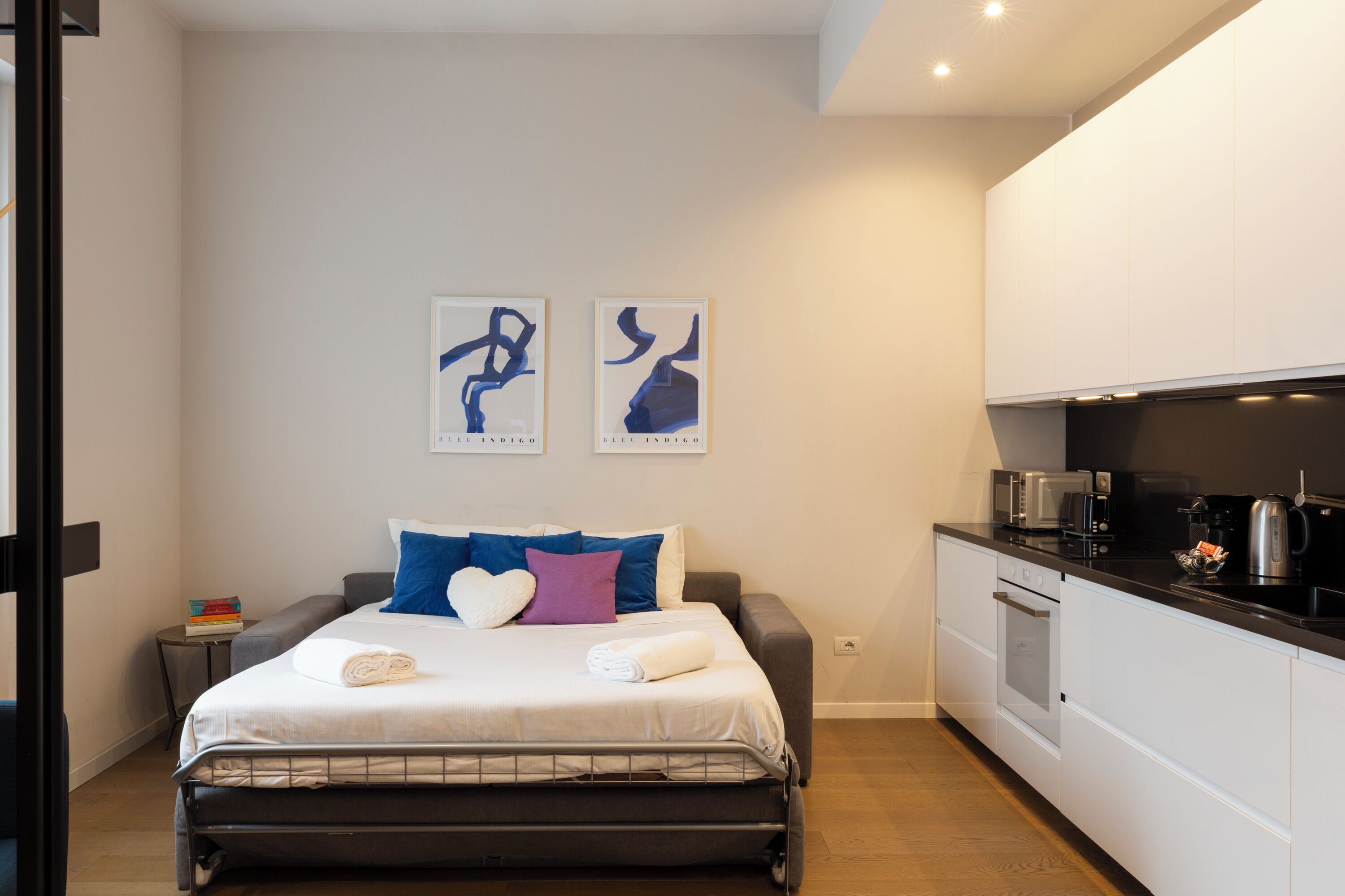 A modern bedroom with a bed, bedside tables, and a kitchenette.