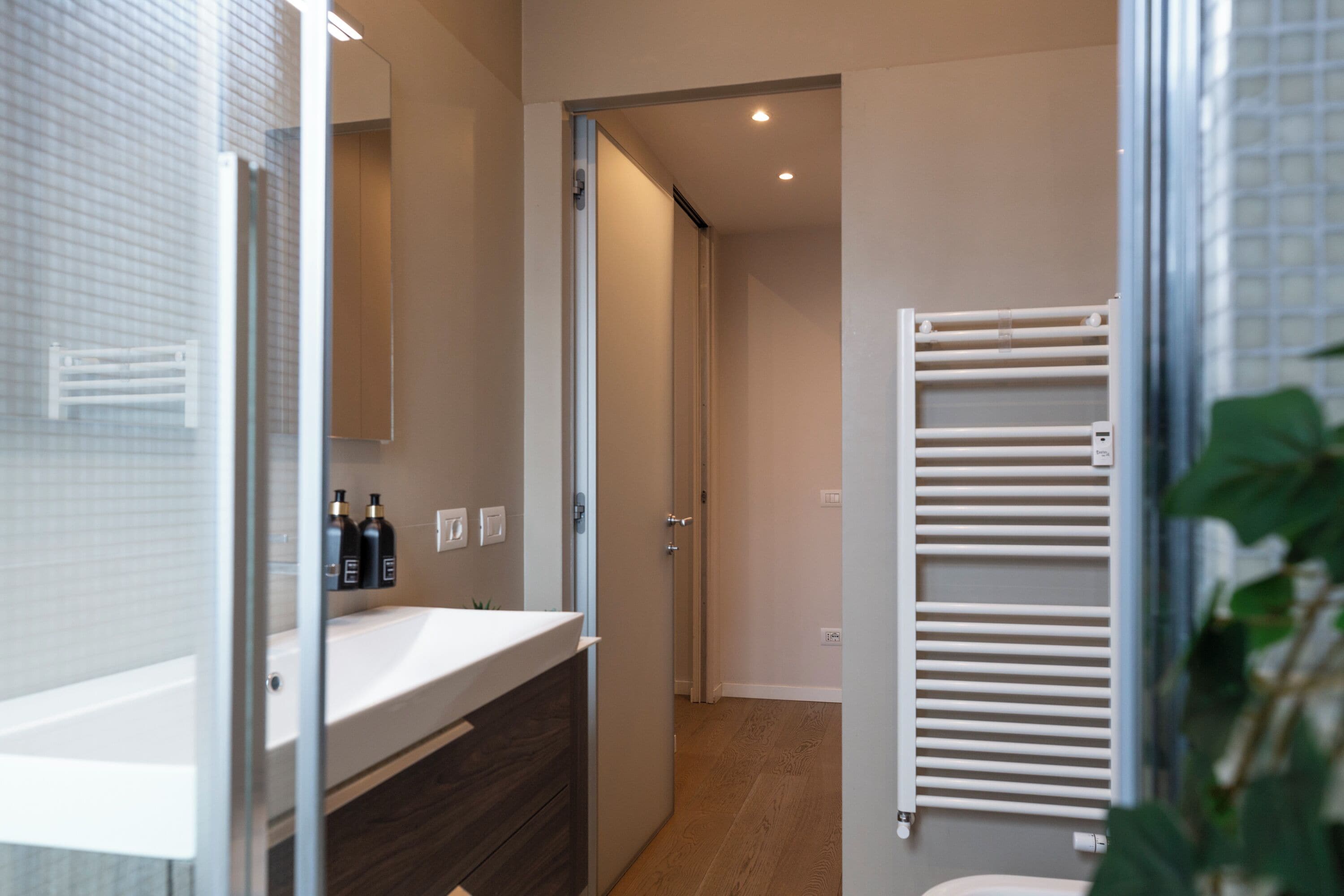 A modern bathroom with a glass shower enclosure, a white sink, and a towel rack.