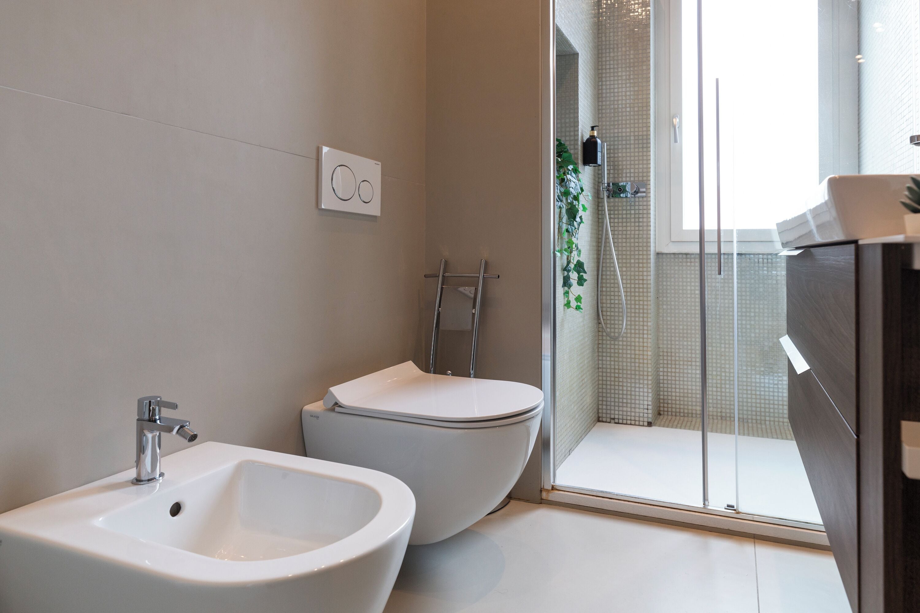 A modern bathroom with a bidet, a sink, and a glass shower enclosure.