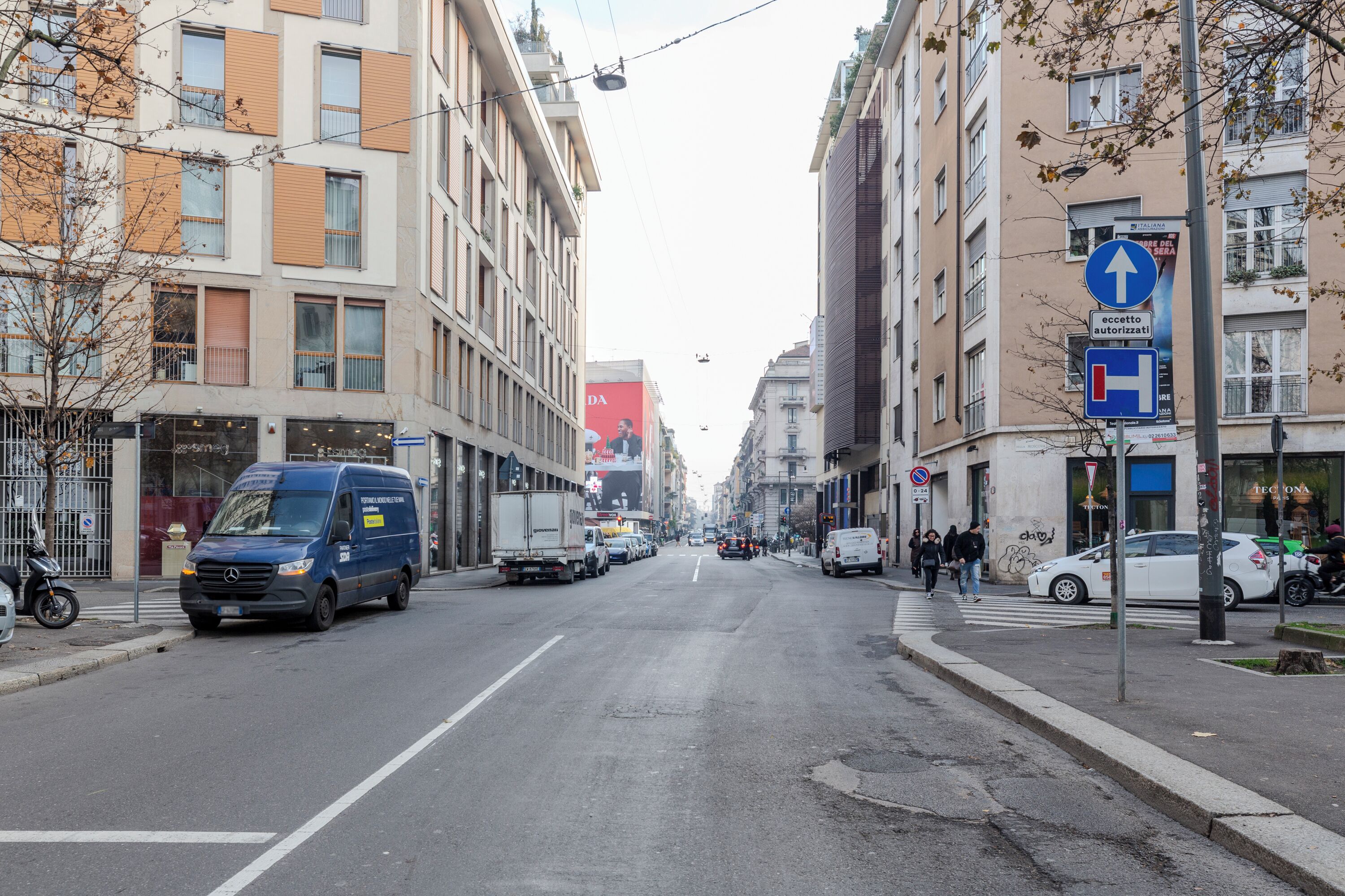 A city street with buildings, parked cars, and a blue van.