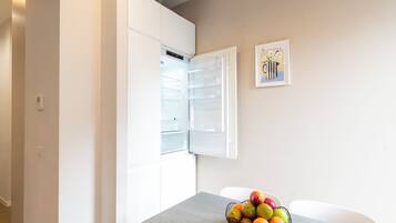 A kitchen with a white refrigerator, a fruit bowl on the counter, and a wall-mounted picture.