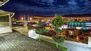 A nighttime view of a cityscape with illuminated buildings, a mosque with minarets, and a river reflecting lights. - Avanos Evi (Avanos)