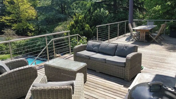 Una terraza con mobiliario de mimbre, una piscina y una mesa con sillas.