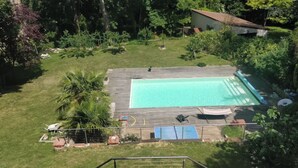 Piscina rectangular con cubierta de madera, rodeada de césped y árboles.