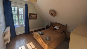 Un dormitorio con cama de madera, una ventana con cortinas, un radiador, una lámpara de pared y un cuadro enmarcado.