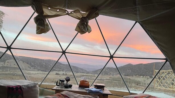 A geodesic dome room with a table, chairs, and a view of a mountainous landscape. - Eagles dôme (Boutferda)