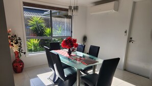 A modern dining area with a glass table, black chairs, and a vase of red flowers. - Tranquil in Alfredton (Alfredton)
