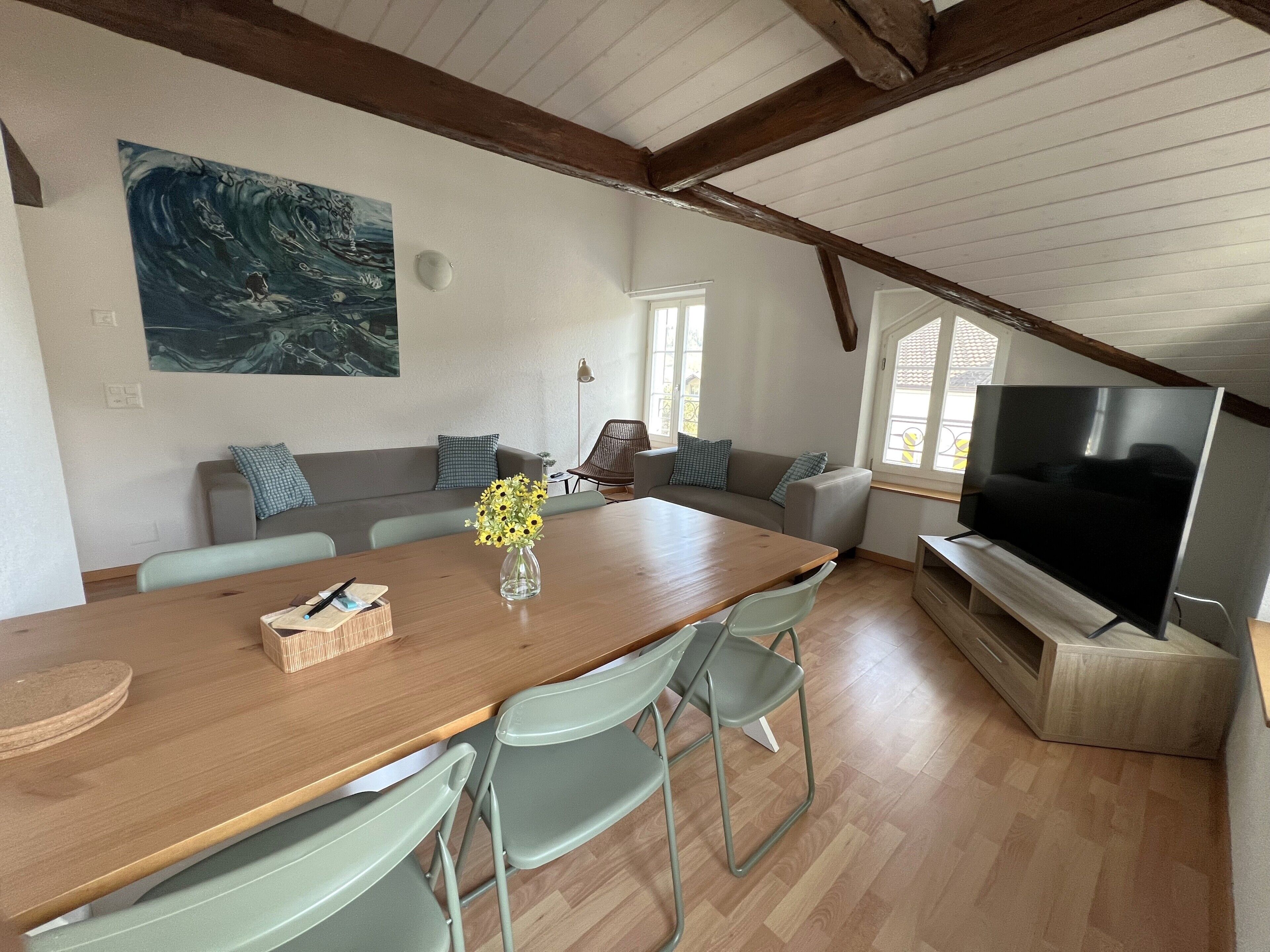 Ein modernes Wohnzimmer mit einem Holzessttisch, grünen Stühlen, einer Couch, einem Fernseher und einem Bild an der Wand.