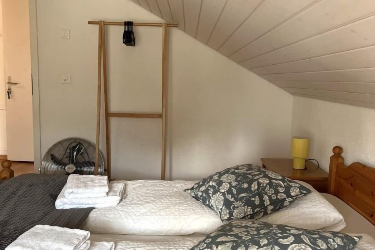 Une chambre à coucher avec un lit, des oreillers, un ventilateur, une table de chevet et une lampe.