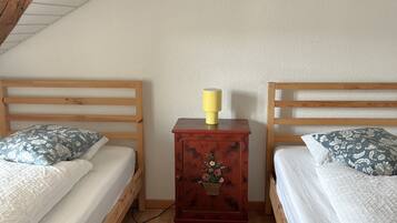 A bedroom with two wooden beds, a small wooden nightstand with a yellow lamp, and a wooden ceiling.