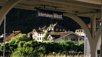 A train station platform with a sign reading 'Interlaken West' and a view of houses in the background.