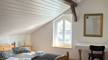 Ein Zimmer mit einem hölzernen Bett, einem Schreibtisch, einem Stuhl, einem Fenster und einem Spiegel.