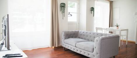 A modern living room with a grey sofa, wooden flooring, a desk, and a TV.