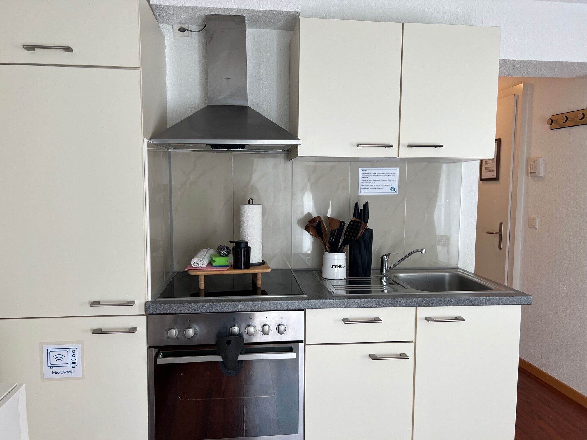 A compact kitchen with a microwave, oven, stainless steel sink, and a utensil holder.