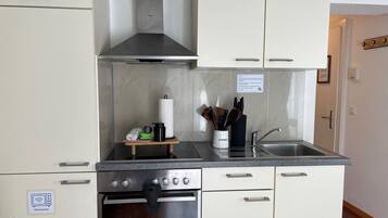 A compact kitchen with a microwave, oven, stainless steel sink, and a utensil holder.