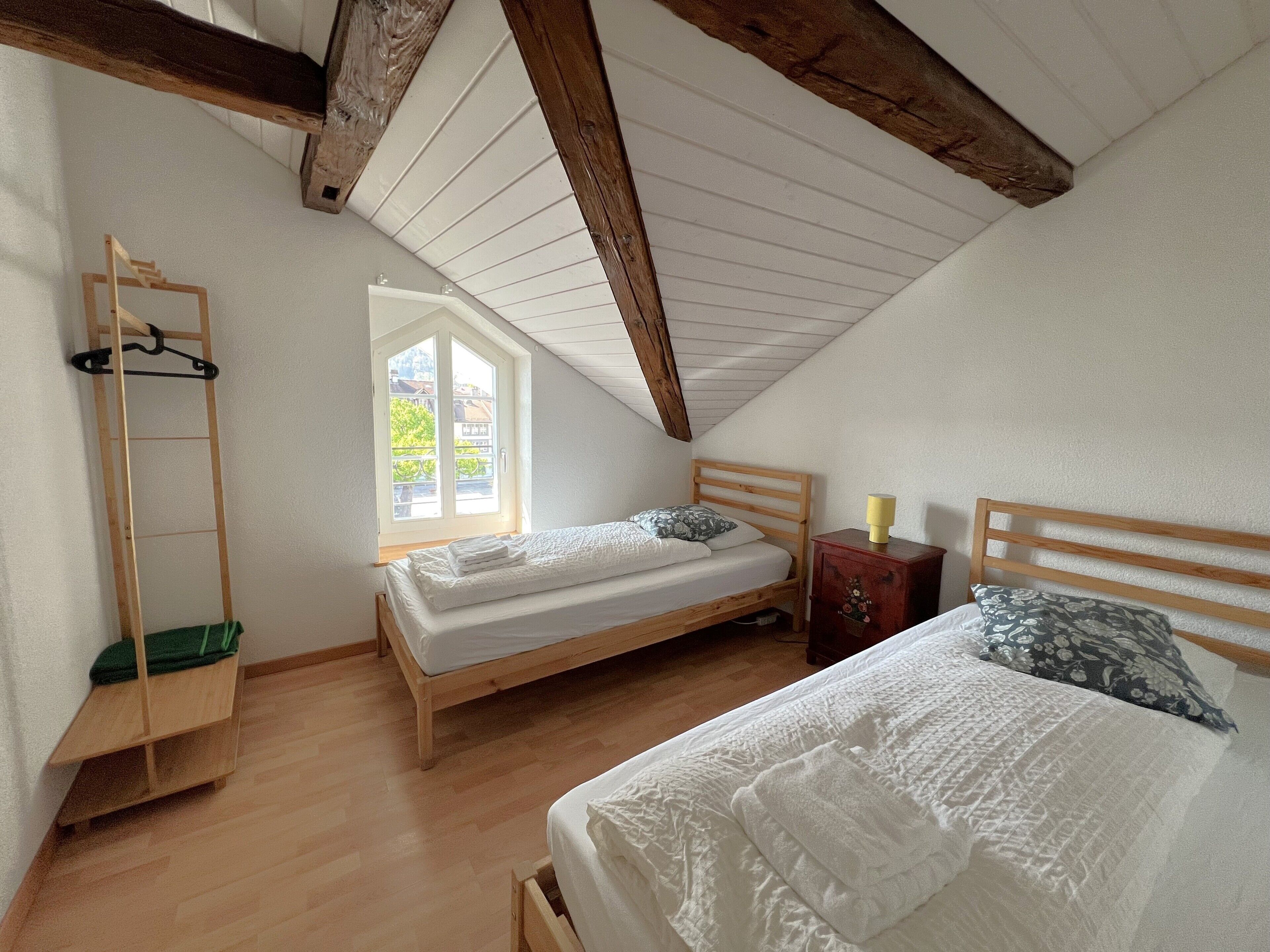 Une chambre avec deux lits, une échelle en bois, une fenêtre et une petite armoire en bois.