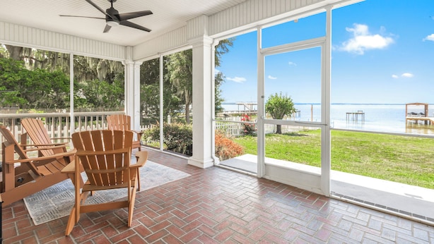 A covered porch with wooden chairs, a ceiling fan, and a view of the water.