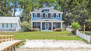 A two-story house with a porch, a grassy yard, and a wooden dock extending into a body of water.