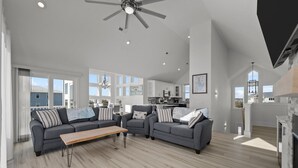 Ein geräumiges Wohnzimmer mit einem großen, grauen Ecksofa, einem Holztisch und einem Deckenventilator.