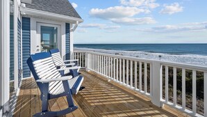 Eine Holzterrasse mit zwei Adirondack-Stühlen, die auf einen Strand ausgerichtet sind.