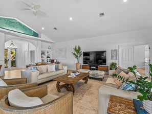 A spacious living room with a large flat-screen TV, comfortable seating, and a ceiling fan.