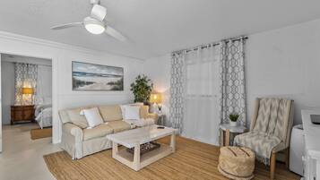 Un salon avec un ventilateur de plafond, un canapé, une table basse, un fauteuil et une lampe.