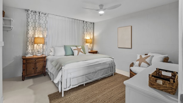 Une chambre à coucher comprenant un lit, des tables de chevet, un ventilateur de plafond et une œuvre d’art accrochée au mur.