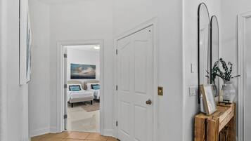 Un couloir avec une porte blanche donnant sur une chambre à coucher, où se trouvent un lit et un tableau.